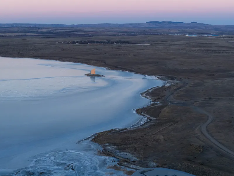 Twilight aerial view showing the illuminated chapel on the frozen lake edge