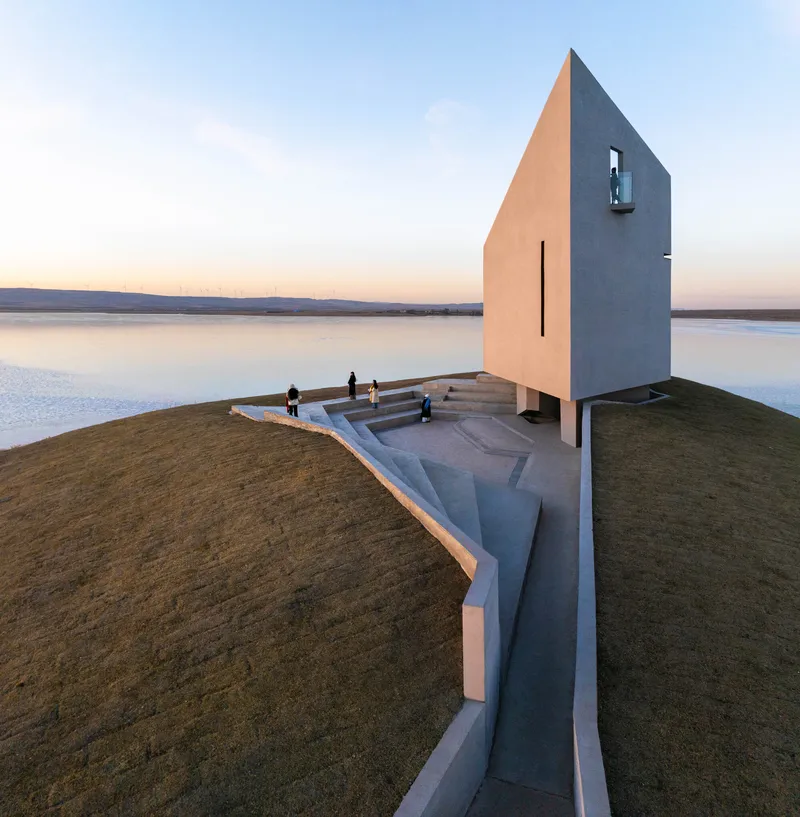 Aerial view of the pentagonal white chapel with concrete terrace and steps extending toward the reservoir at dusk