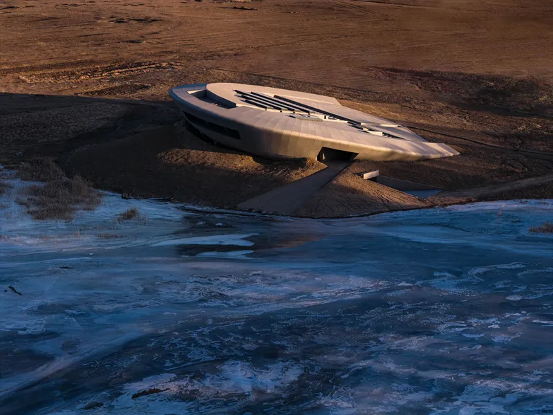 Aerial view of the curved concrete roof set on a peninsula between frozen wetlands at golden hour