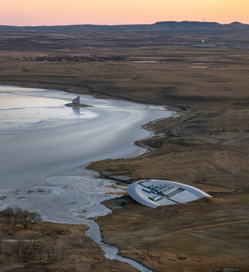 Distant view of two structures positioned along the ice-covered water's edge at sunset