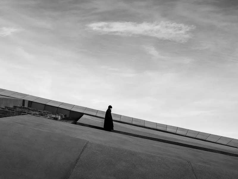 Black and white photograph of a single figure walking along the sloped concrete roof