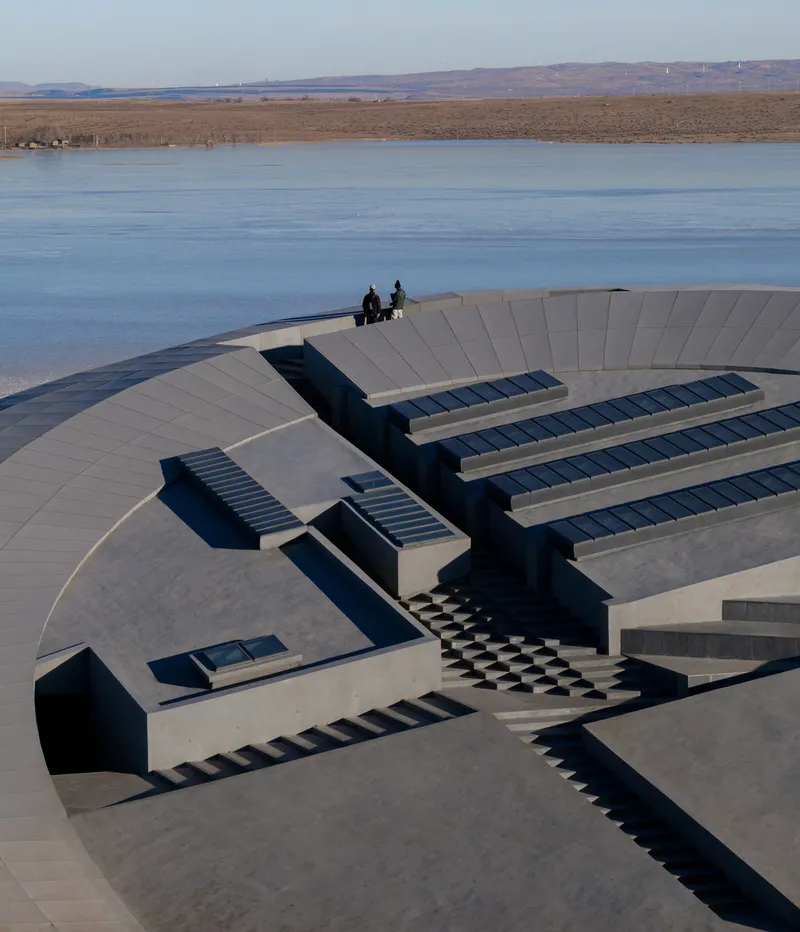 Concrete terraced roof with skylights and two figures standing at the highest platform overlooking the lake