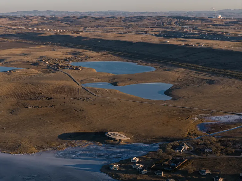 Wide aerial perspective showing the building among multiple water bodies in the rolling dry landscape