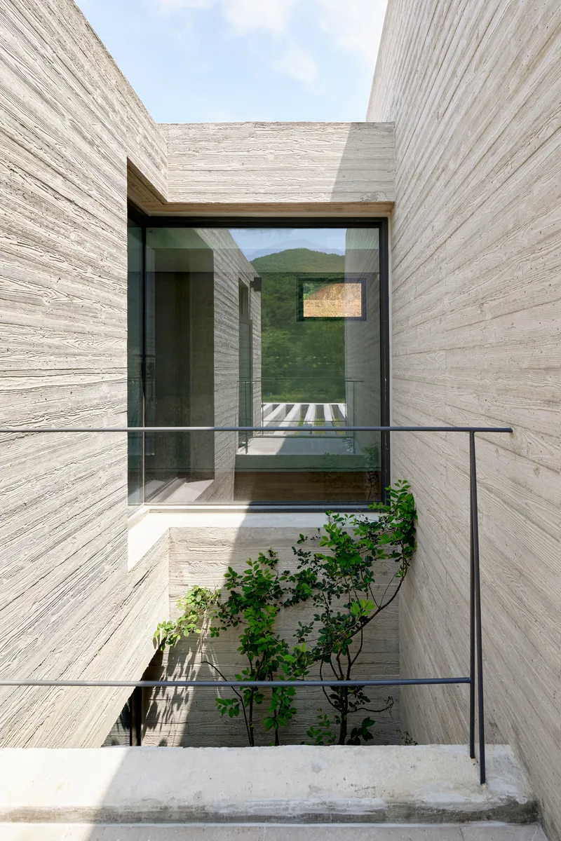 Concrete entry courtyard with glass bridge and planted tree beneath the mountain view