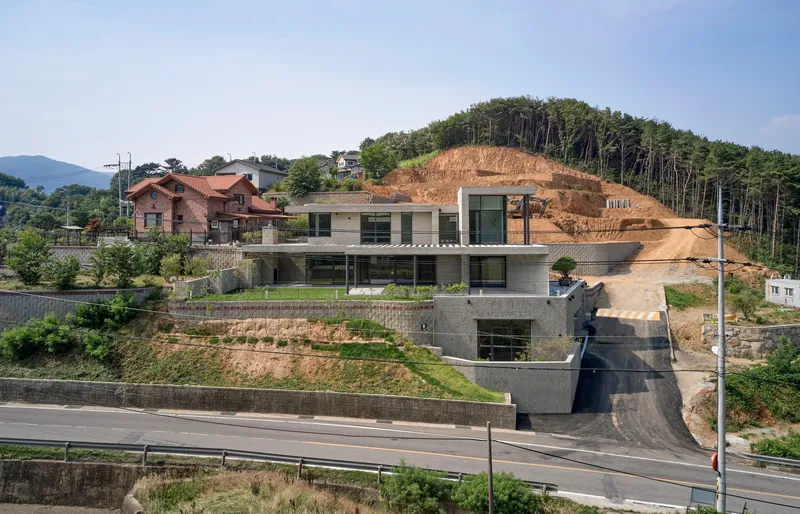 Hillside site showing the three-level house carved into the slope beside the highway