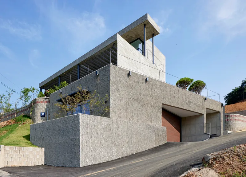Street facade showing textured concrete walls with garage openings and cantilevered upper levels under clear sky