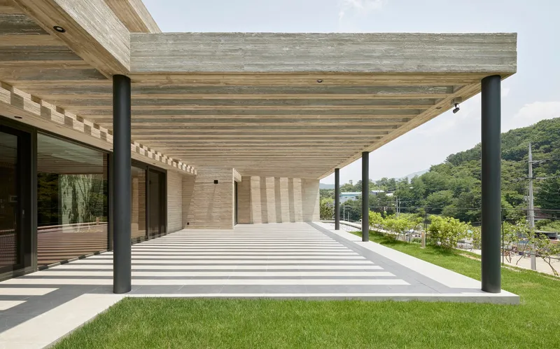 Covered terrace with exposed timber slat ceiling supported by black steel columns overlooking grass lawn