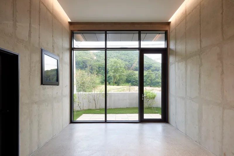 Entry vestibule with board-formed concrete walls and full-height glazed door framing hillside view beyond courtyard