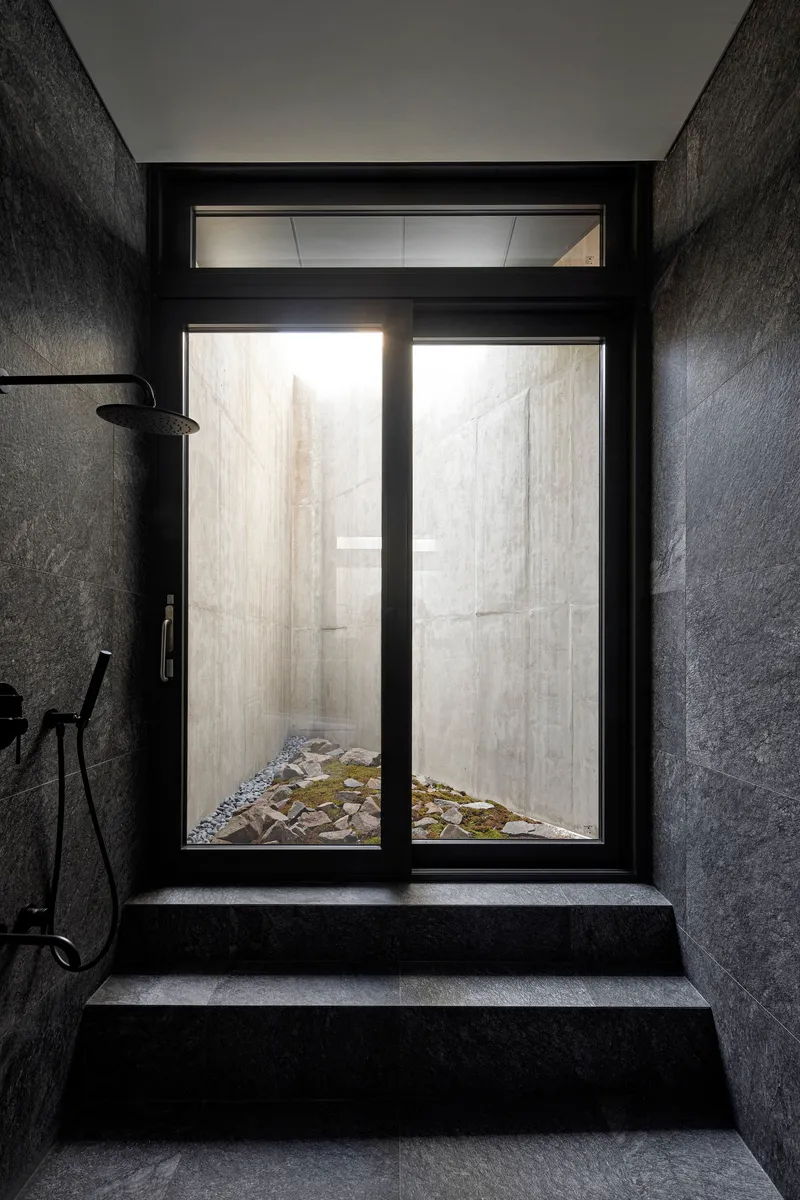 Dark stone shower room with glazed door opening onto a planted courtyard with rocks and moss
