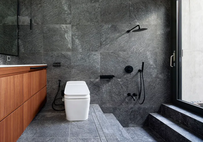 Bathroom with charcoal stone tile walls, timber vanity, and black shower fixtures beside a glazed door