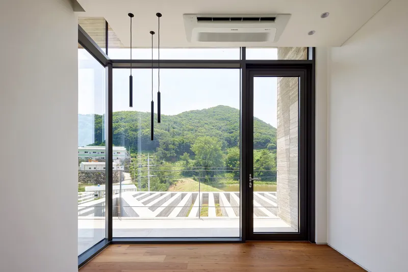 Interior room with timber floor and black-framed glazing overlooking a slatted deck and forested hillside