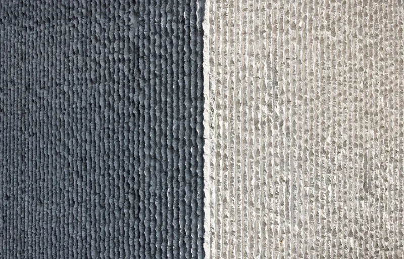 Close-up of two textured concrete panels showing dark grey and light grey ribbed formwork patterns