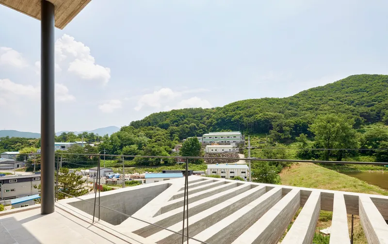 Rooftop terrace with glass balustrade overlooking striped concrete seating steps and forested hillside