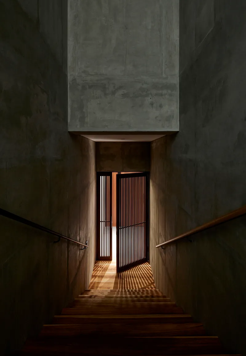 Interior staircase descending toward timber slat door with light filtering through at dusk