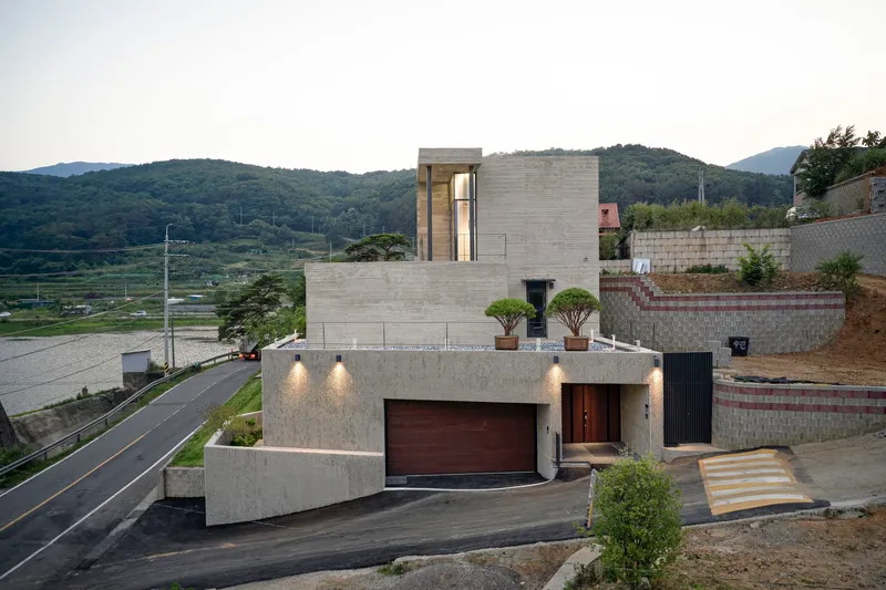 Board-formed concrete facade with timber garage door and entrance canopy lights at twilight