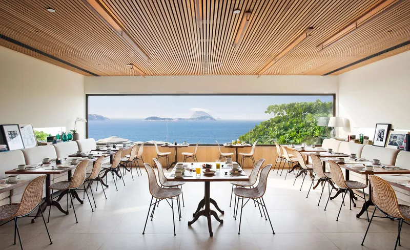 Dining hall with timber slat ceiling framing a panoramic ocean view through a horizontal window