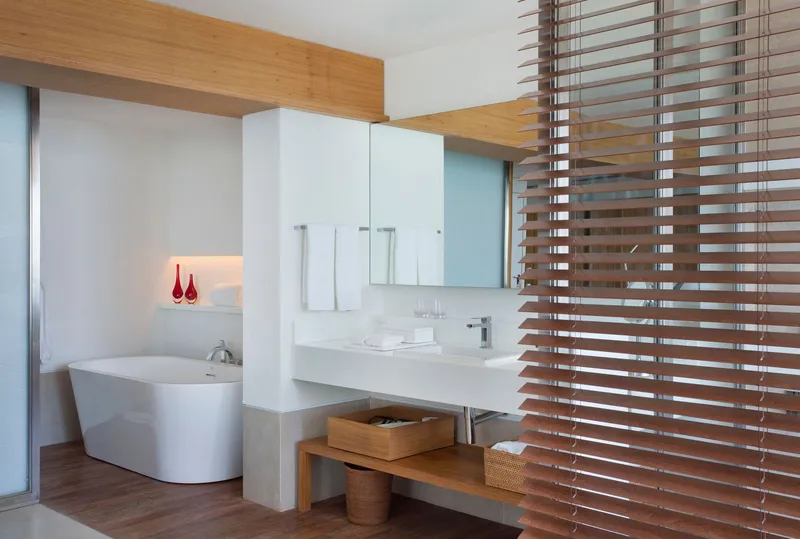 Bathroom with freestanding white tub separated by a wood slat screen from the vanity