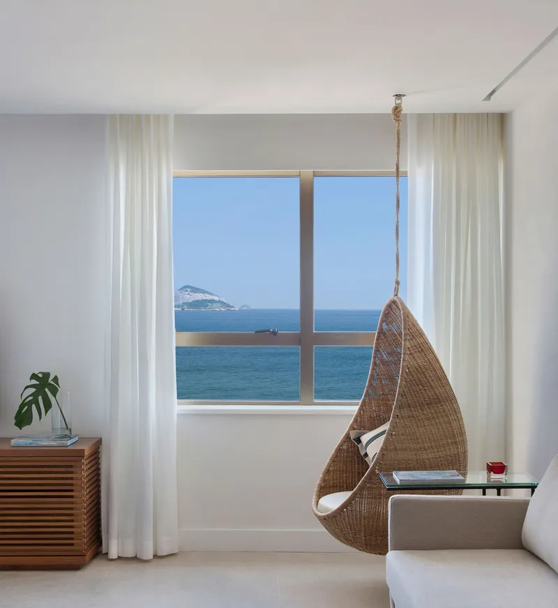 Window seat nook with suspended wicker chair and ocean view through sheer white curtains