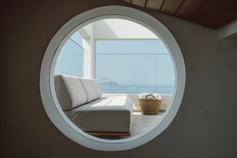 Circular window framing a terrace with daybed and ocean vista beyond