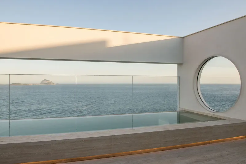 Rooftop terrace with circular portal and glass-edged pool facing the open sea at dusk