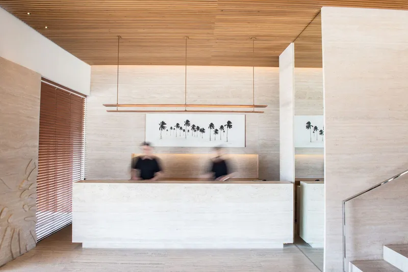 Reception desk with horizontal timber ceiling and blurred figures beneath linear pendant lighting