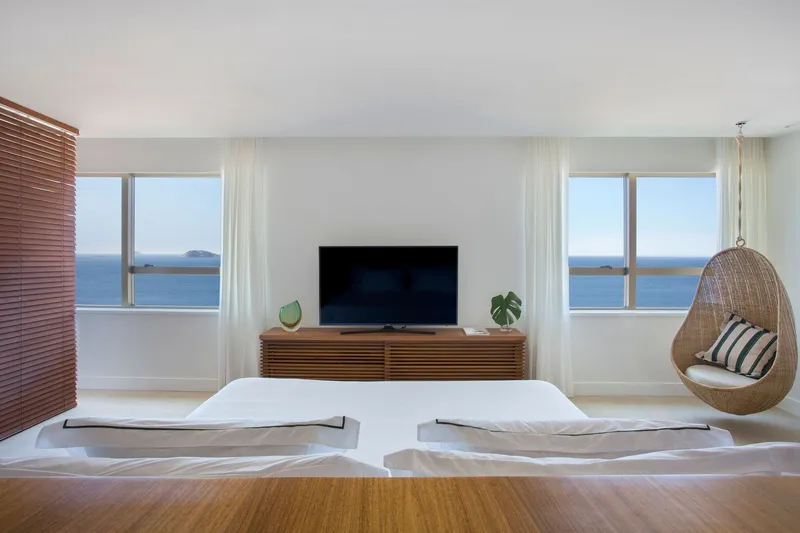 Bedroom with twin windows framing the ocean and a hanging wicker chair