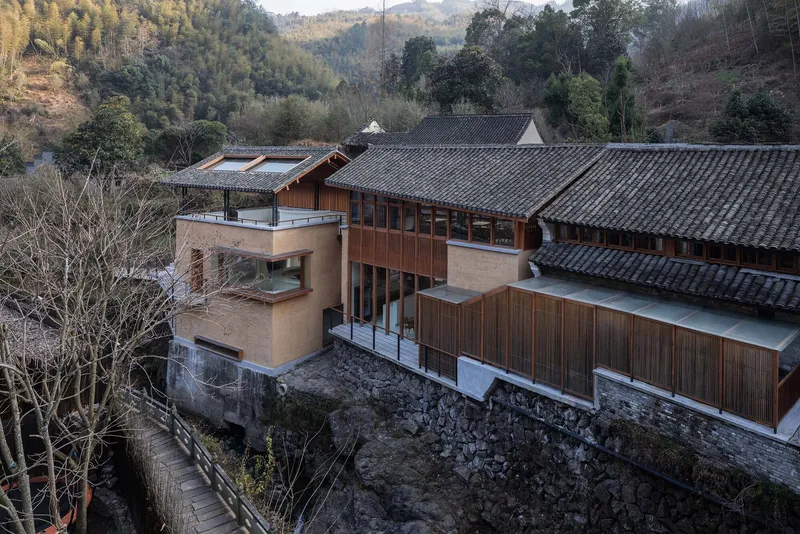 Elevated view showing timber and stucco volumes atop a stone retaining wall among bare trees
