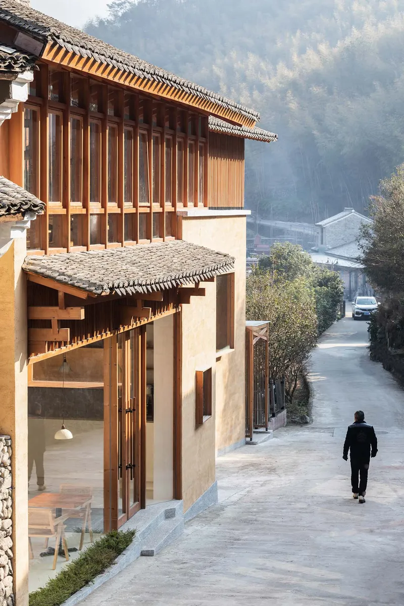 Street-facing facade with vertical timber slats and tiled canopy as a figure walks away