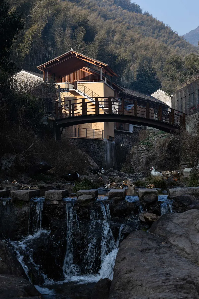 The timber upper story and rammed earth lower volumes spanning the cascading waterfall and rocky streambed