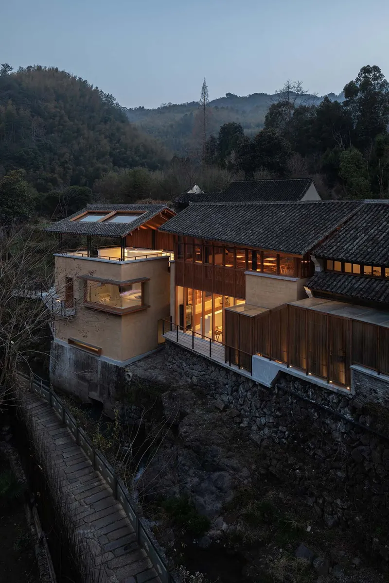 Elevated view of the rammed earth and timber volumes with tiled roofs nestled among neighboring structures at dusk