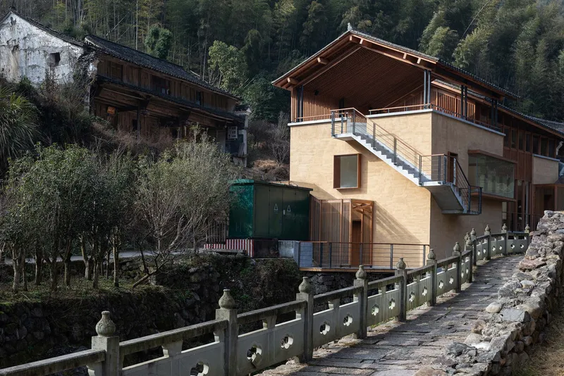 Daytime view of the rammed earth tower with external stair beside a carved stone balustrade and green utility box