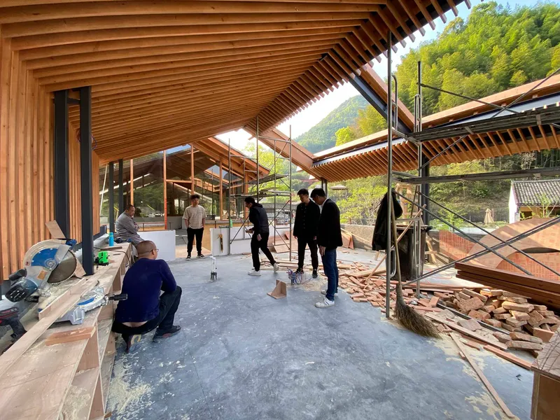 Interior view of the timber-slatted ceiling and glazed walls during construction with workers present
