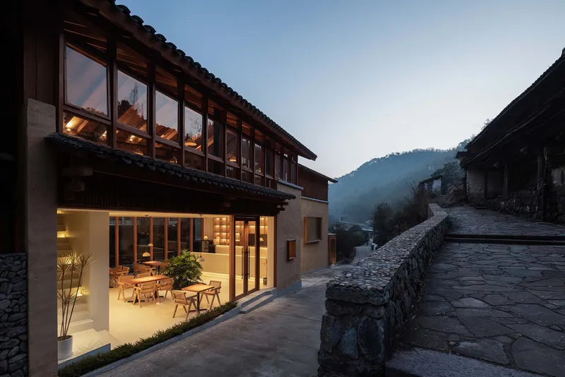 Two-story facade with recessed terrace and full-height windows opening onto flagstone courtyard in morning mist