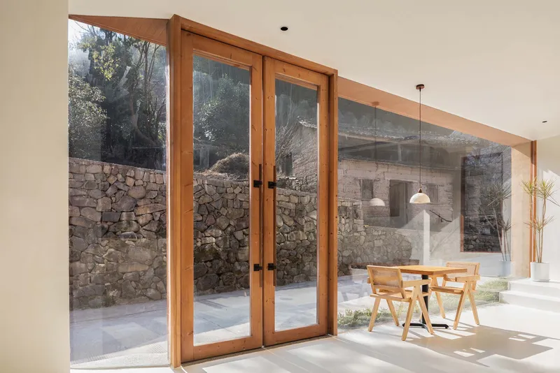 Timber-framed glazed doors opening to a courtyard with stone walls in bright daylight