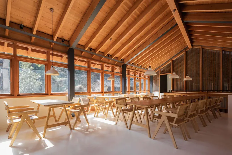 Dining hall with exposed timber rafters, continuous glazing, and rows of timber chairs
