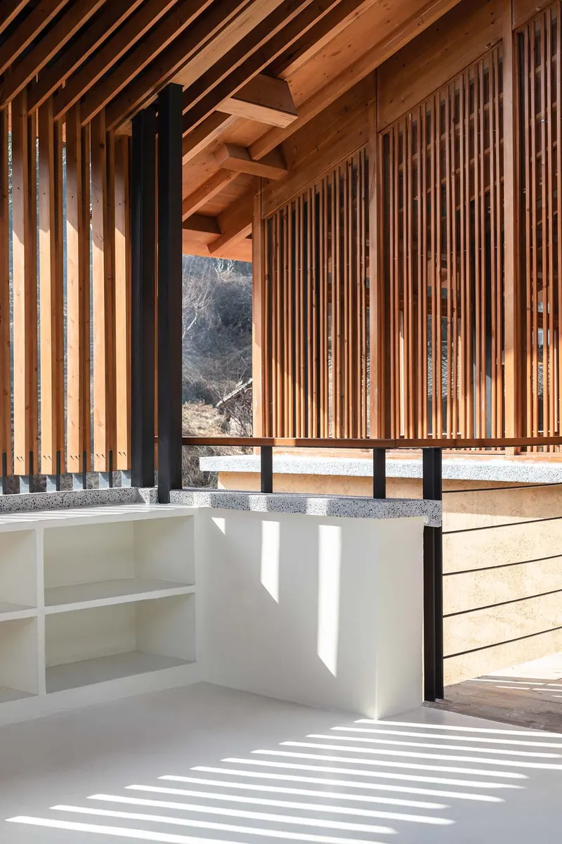 Covered terrace with timber slat screens and exposed rafters casting diagonal shadows across white flooring