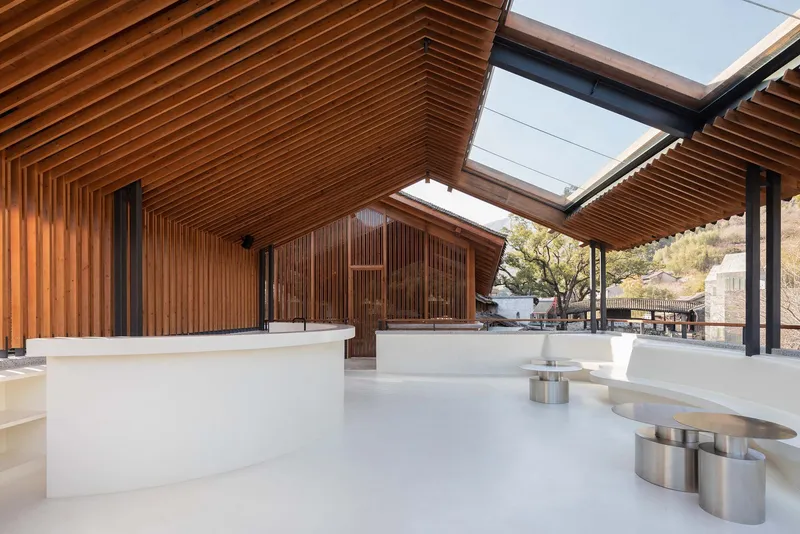 Open-air pavilion with timber louvered ceiling and skylights above white terrazzo seating platforms