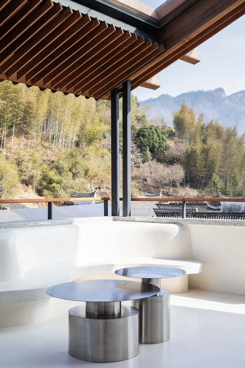 Brushed steel low tables on white terrace overlooking forested hillside in daylight