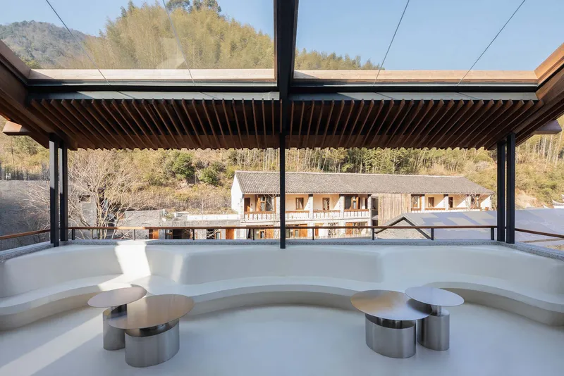 Curved white seating alcove under slatted timber canopy with village rooftops visible beyond