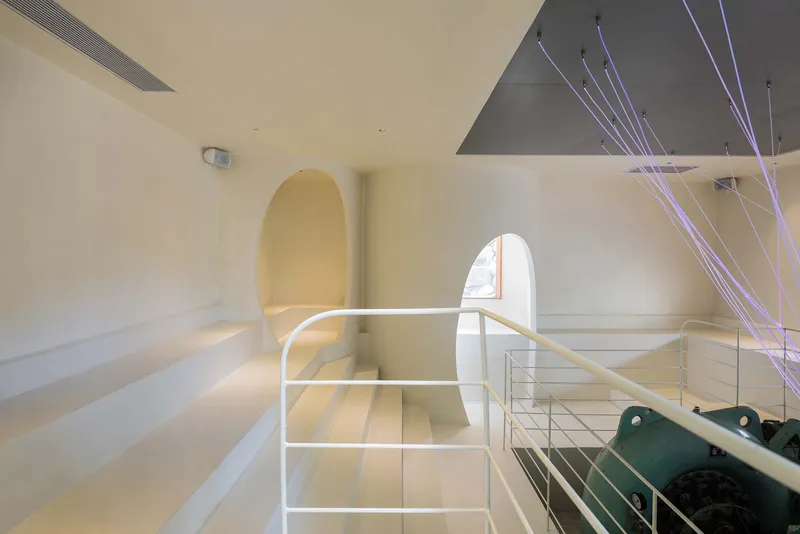 Interior view of white tiered seating with arched doorway and suspended cable lighting from above