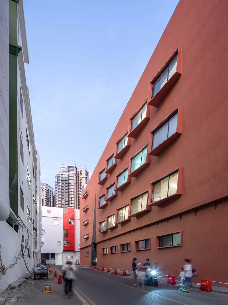 The terracotta facade with recessed windows at dusk with pedestrians and scooters passing through the alley