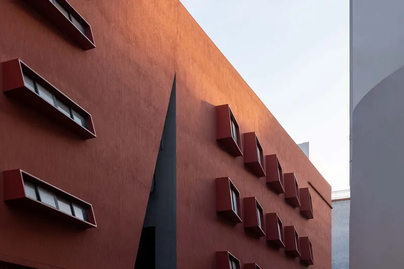 Close-up of the terracotta facade with angled window boxes in two rows and a dark vertical skylight slot
