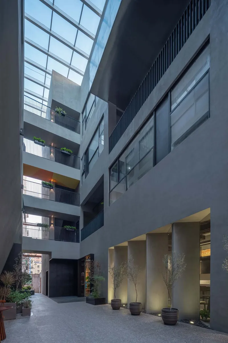 Interior atrium courtyard at dusk with glass skylight, residential balconies and illuminated ground-floor planters