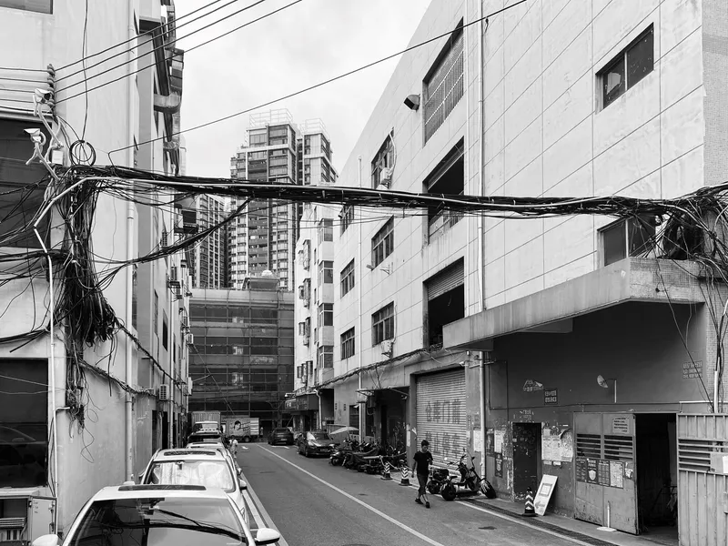 Narrow urban alley with tangled overhead wires, parked cars and surrounding concrete apartment blocks