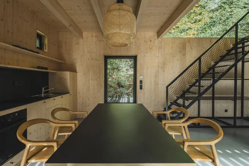 Long dining table with bentwood chairs beneath woven pendant facing doorway to exterior