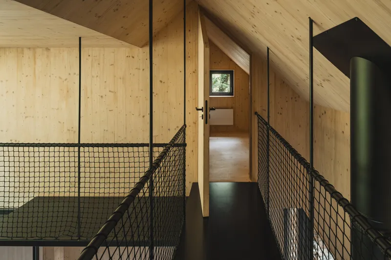 Interior walkway with black mesh railings and plywood walls under an exposed timber ceiling