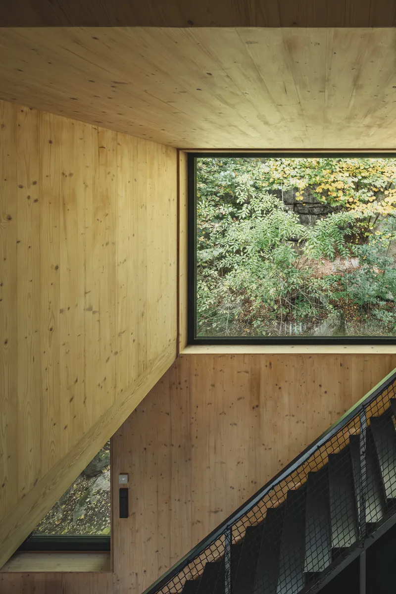 Stairwell corner with plywood paneling and a large window framing vegetation outside