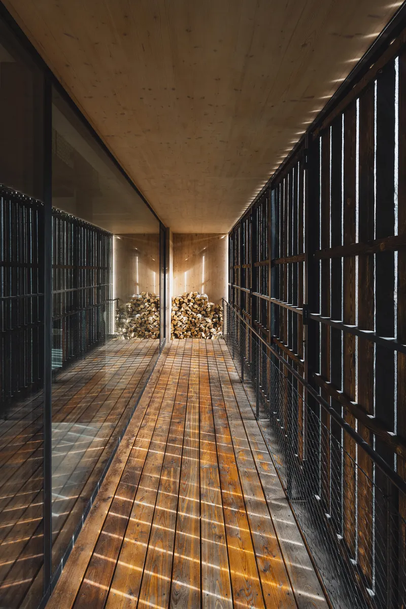 Enclosed walkway with timber decking and vertical black slat screens filtering afternoon light