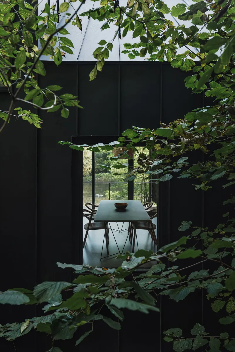 View through tree branches toward a dining area framed by black metal panels