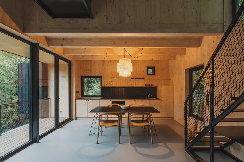 Dining area with exposed timber beams and plywood walls opening to deck through sliding doors